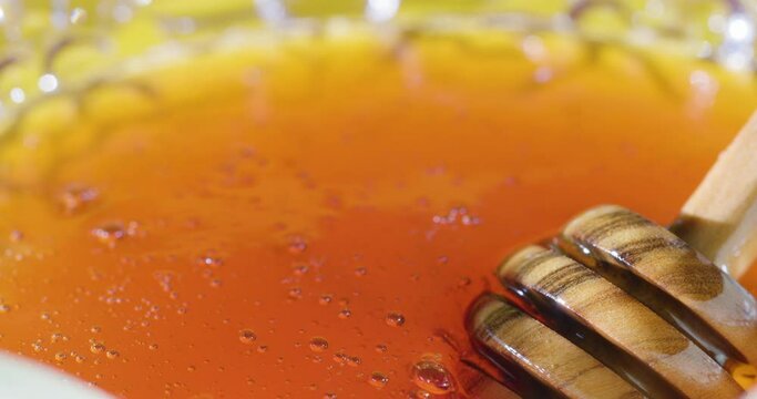 A honey spoon is lowered into a jar of honey and scoops up the honey.