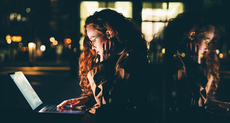 Woman using laptop on night city street.