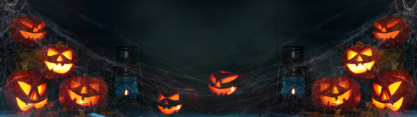 Scary Halloween celebration holiday background banner panorama - Spooky pumpkins, lantern candle and spider web in the dark night sky with dust © Corri Seizinger