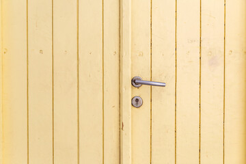 Wooden closed empty beige door, silver metal knob, keyhole background, texture. Greek island