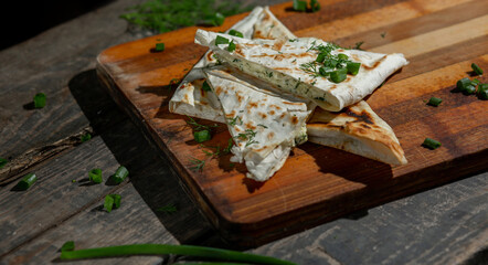 A dish of cottage cheese with parsley and onions in pita bread fried on a grate lie on a board