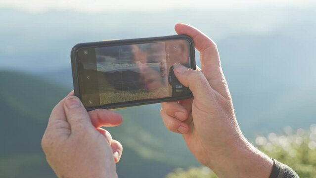 Close-up of phone in hand, while photographing landscape, mountain nature, male hands on sunny day. Photo on the phone. High quality 4k footage