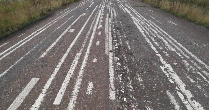 There are a lot of white markings, solid and discontinuous lines on the old paved road. A training place for applying white road markings. A first-person view of moving forward.