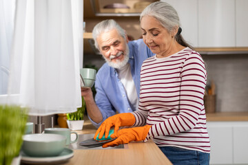 Household Concept. Smiling Senior Husband And Wife Washing Dishes Together In Kitchen