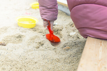 Children's hand with a plastic scoop plays in the sandbox, close-up