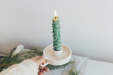 Hand holding stylish christmas candle as fir tree on background of white rustic table. Handmade...