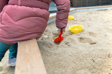 Children's hand with a plastic scoop plays in the sandbox, close-up