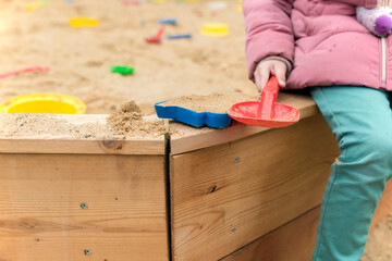 Children's hand with a plastic scoop plays in the sandbox, close-up
