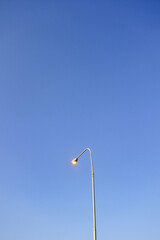 tall lit metal street lamp under bright blue clear sky	
