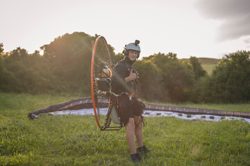 Young man, with the Powered Paragliding engine in his shoulders, gets ready to fly at sunset. Look...