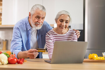 Fototapeta na wymiar Senior Couple Ordering Groceries Online With Laptop And Credit Card In Kitchen