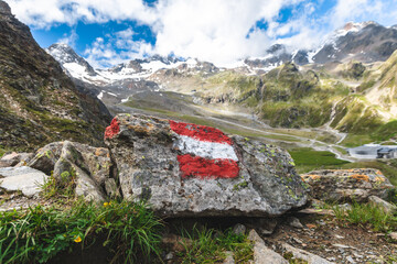Alpine hiking trail in Austria, marked with a painted Austrian flag on a rock along the route. This painted rock is located in the Valley of Stubai, in the Austrian Tyrol.