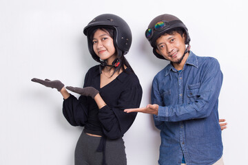 Young asian couple with a motorcycle helmet pointing with fingers to different directions isolated on white background