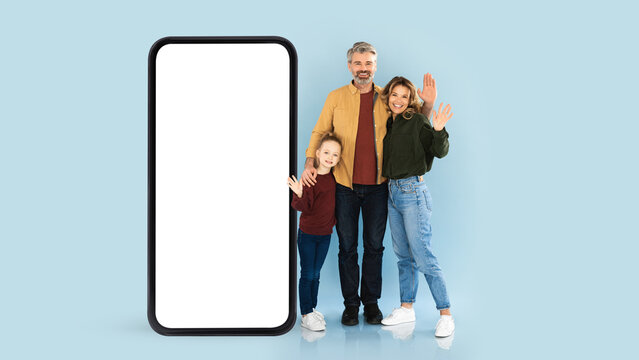 Happy Family Of Three Standng Near Big Blank Smartphone With White Screen