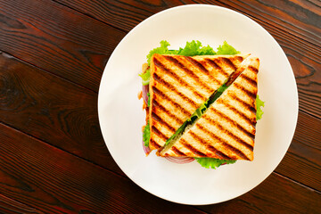Homemade club sandwich with toasted bread slices, chicken breasts, tomato, salad leafs, cucumber, onion on white plate. On wooden tabletop. Flat lay. 