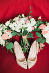 Pair of elegant and stylish bridal shoes with wedding rings and a bouquet of roses and other flowers
