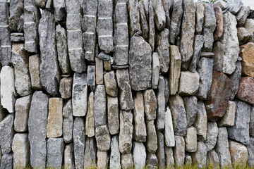 A horizontal image of stones in a dry fence.  There are many that make up the design in mostly granite with other color’s standing out like red or yellow.  