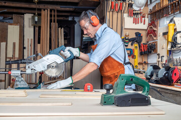 CARPENTER IN WORKSHOP WORKING WOOD WITH A MITER SAW. DIY AND PPE CONCEPT. PERSONAL PROTECTION...