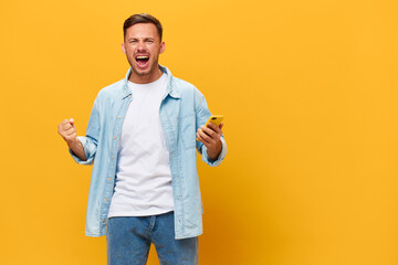 Angry irritated tanned handsome man in blue basic t-shirt scream at camera hold phone posing isolated on orange yellow studio background. Copy space Banner Mockup. Online Social media concept