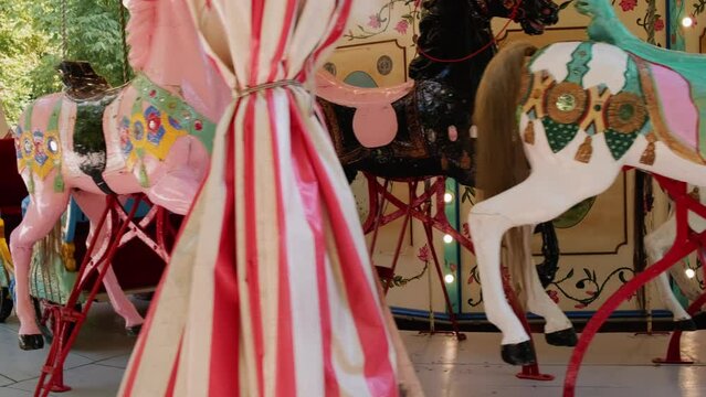 Multicoloured horses on old fashioned French carousel in amusement park on sunny day. Empty merry-go-round with lights waiting for children