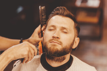 Barbershop concept vintage toning. Barber shearing beard to man in hair salon