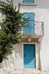 Old historic Italian architecture. Blue wooden door, balcony, blooming bush, white walls with sunlight shadows