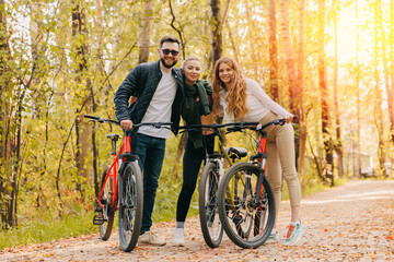 Obraz premium Happy friends together two woman and man cycling in autumn city park. Concept active rest weekend