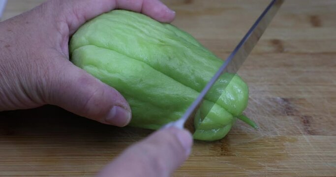 Female hands starting to cut a tip of a chayote with a knife on a cutting board for the kitchen, known as: labu siam, jipang, organically grown vegetables. Healthy homemade food concept