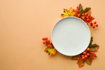 Fall table setting. White plate and fall decorations at orange background. Flat lay image with copy...