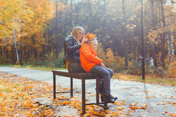 Single parent mother and child boy in the autumn in park sit on bench. Fall season and family...