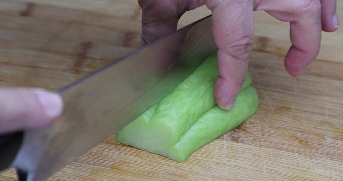Adult female hands slicing and cutting a chayote with a knife on a wooden cutting board for the kitchen, known as: labu siam, jipang, organically grown vegetables. Healthy homemade food concept