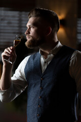 A male sommelier is tasting a drink in a glass.