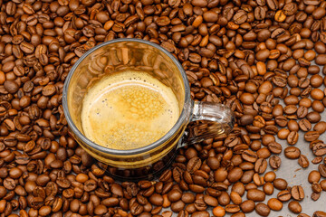 Espresso coffee in glass cup with coffee beans on wooden table.
