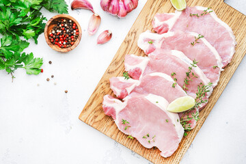Raw pork chops, meat on cutting board prepared for cooking with garlic, thyme and pepper. White kitchen table,  top view