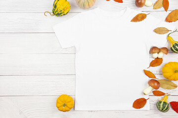 White womens cotton t-shirt mockup with pumpkins, mushrooms and fallen leaves on white wooden background. Design t shirt template, print presentation mock up. Top view flat lay.