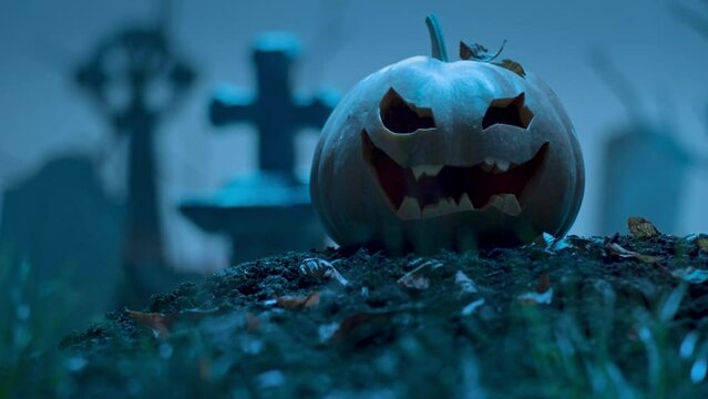 Glowing Halloween pumpkin among the graves in the cemetery. Holiday event halloween concept.