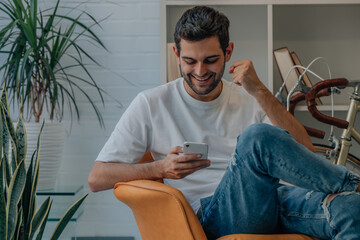 young man at home euphoric celebrating looking at mobile phone