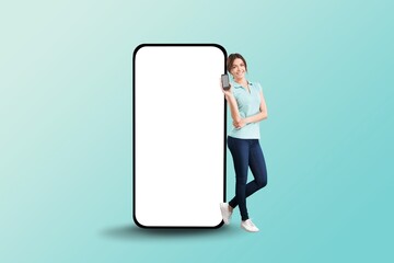 Young smiling happy woman stand near big mobile cell phone with blank screen
