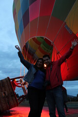 Latin couple of man and woman celebrate their anniversary before boarding a hot air balloon show their love with kisses, hugs and sign of freedom and victory

