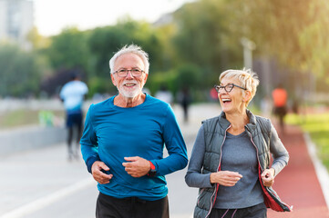 Cheerful active senior couple jogging together outdoors along the river. Healthy activities for...