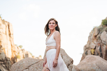 Confident woman with red hair and a white flowy outfit stands outdoors in the mountains with elegance