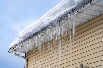 Sharp spiked icicles on roof with snow against blue sky. Icicles on roof of private house resulting...