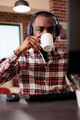 Young adult working from home on computer and listen to music or podcast show online on headphones....
