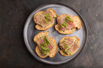 Bread sandwiches with jerky salted meat, sorrel and cilantro microgreen on black. top view.