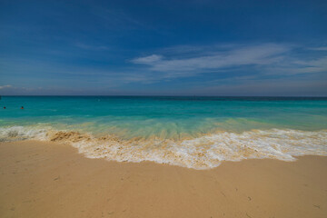 Fototapeta na wymiar Beautiful view of rolling turquoise wave on sandy beach in Atlantic ocean on island of Aruba.