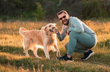 Handsome man with a dog golden retriever walk in autumn meadow
