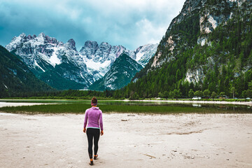 Young woman walks at sand beach during a rainy noon. Dürrensee (Lago di Landro), Saint Ulrich, Dolomites, Belluno, Italy, Europe.