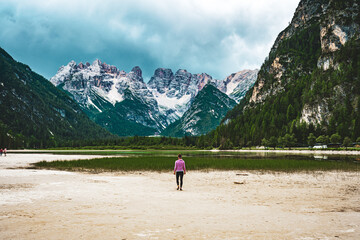 Young woman walks at sand beach during a rainy noon. Dürrensee (Lago di Landro), Saint Ulrich, Dolomites, Belluno, Italy, Europe.