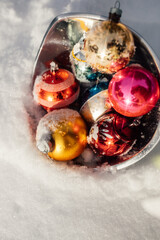 silver bowl sitting in the snow, full of vintage pink, gold, red, blue Christmas tree ornaments 
