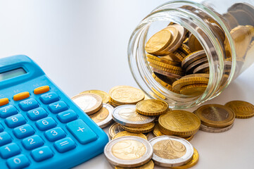 Calculator, with a jar of coins beside it. Savings and payment of monthly expenses.